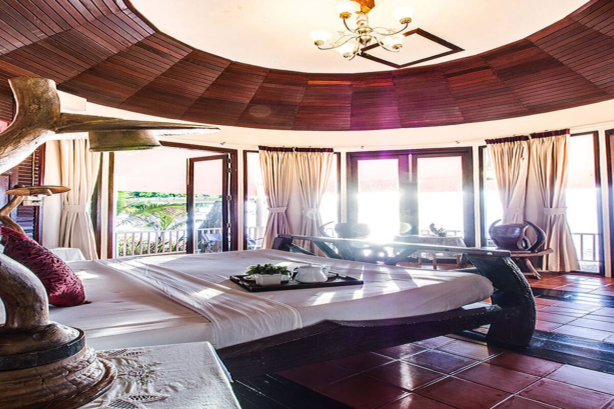 A spacious bedroom with a large bed, a wooden ceiling, and a view of the outdoors.