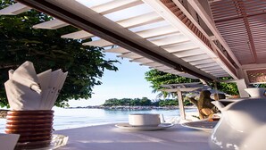 A table set with white tableware and a napkin holder, overlooking a body of water with a view of a distant island. - Sans Souci Samui (Koh Samui)