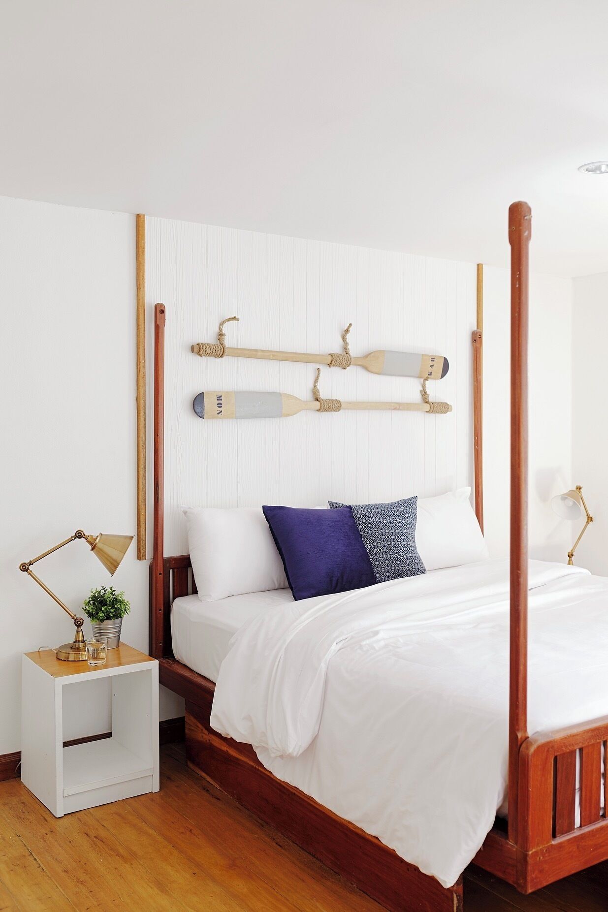 A four-poster bed with a white headboard, a bedside table with a lamp, and a potted plant.