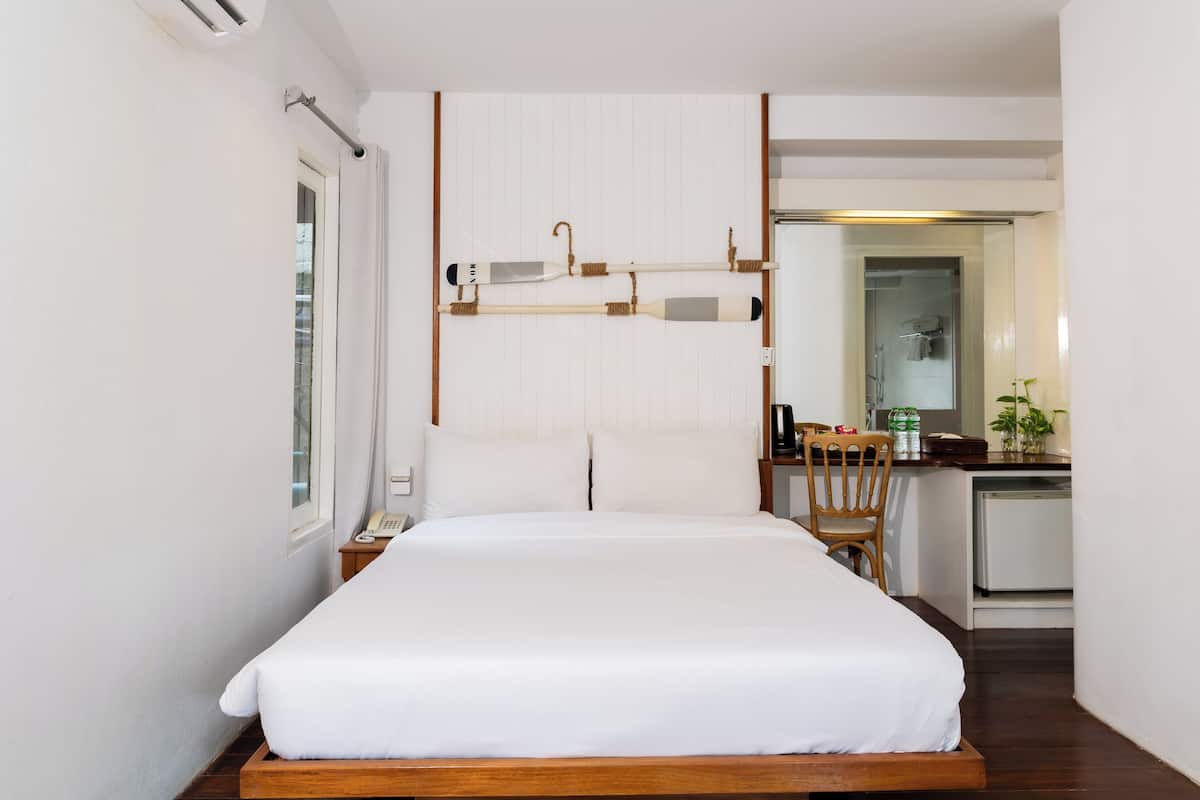 A hotel room with a bed, a small desk with a chair, a window, and a door.