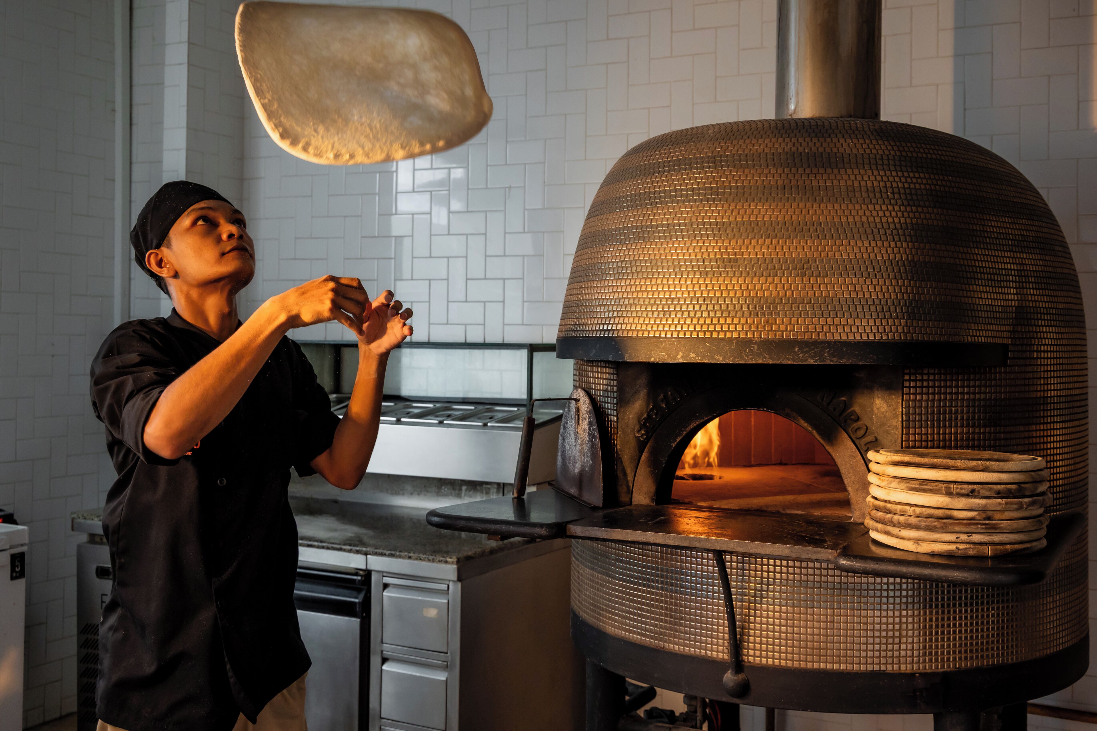 Iemand bereidt eten in een keuken met een bakoven, betegelde spatwand en moderne apparatuur.