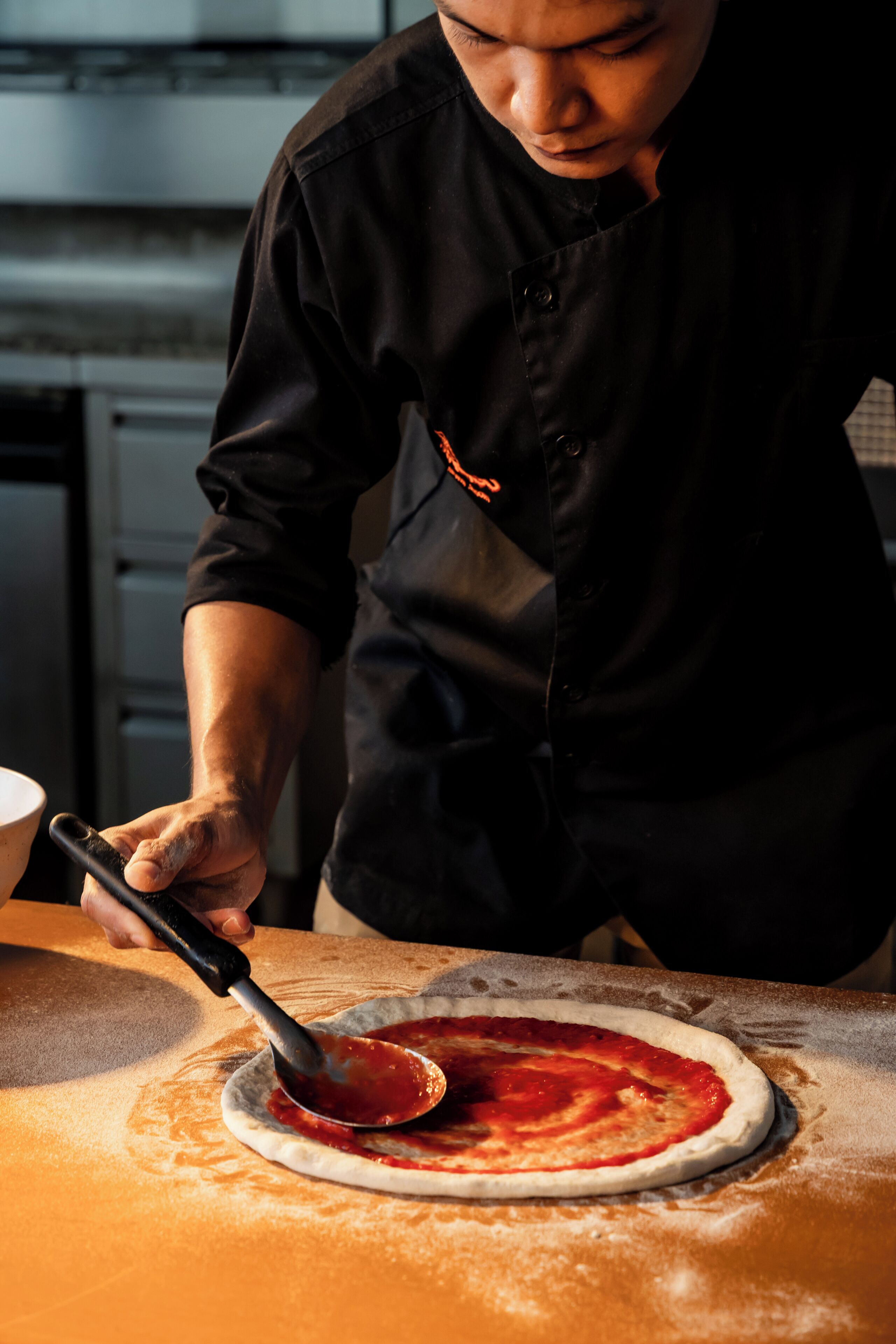 Uma pessoa preparando pizza sobre uma mesa com superfície de madeira.