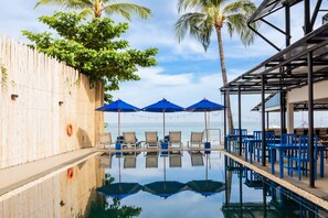 A pool area with lounge chairs, blue umbrellas, and a wooden fence. - Malibu Beach Resort Samui (Koh Samui)