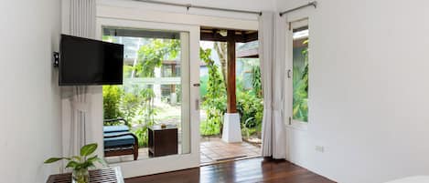 A modern bedroom with a TV, a small table with a plant, a bed, and a sliding glass door leading to a garden.