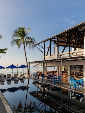 A beachfront bar with outdoor seating, a pool, and a view of the ocean.