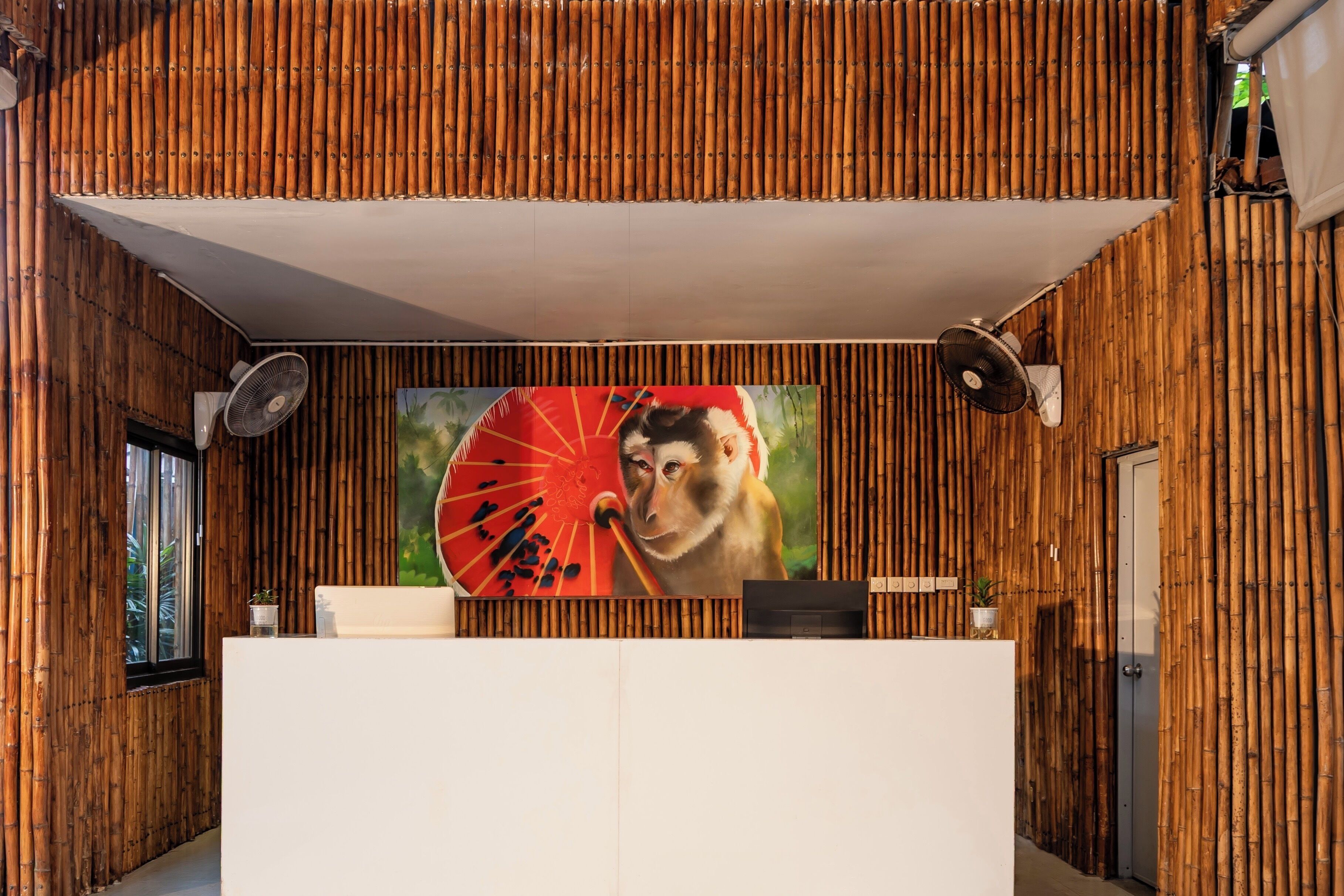 A reception area with a bamboo wall, a large painting of a monkey holding a fan, and a reception desk.