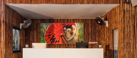 A reception area with a bamboo wall, a large painting of a monkey holding a fan, and a reception desk.
