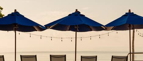 Un espace aménagé avec des parasols et des chaises, situé au bord de la plage et donnant sur l’océan.