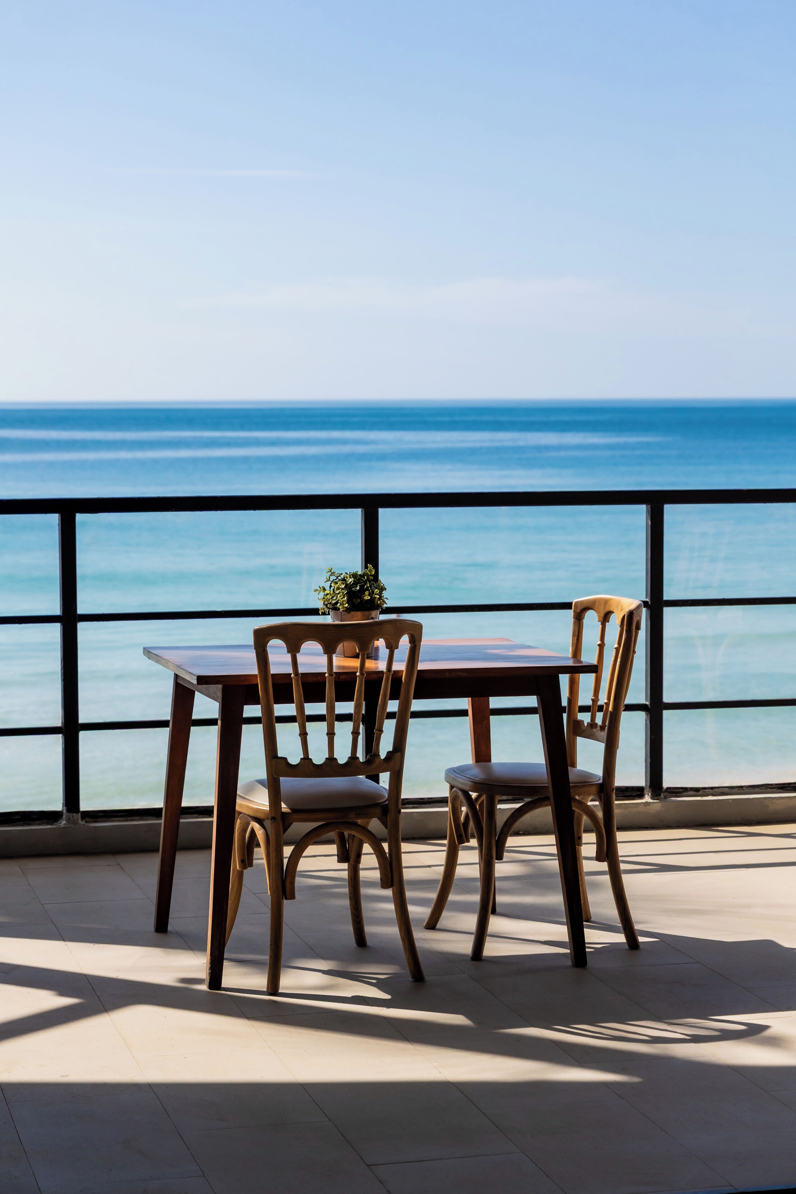 A wooden table and chairs on a balcony with a view of the sea.
