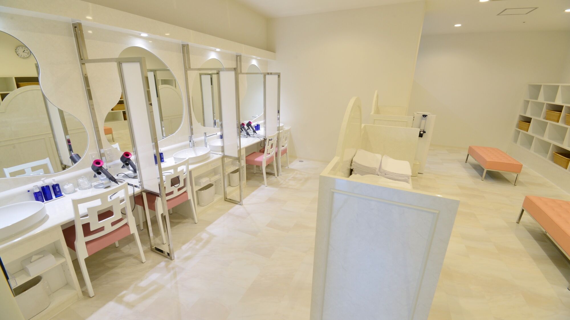 A modern bathroom with multiple sinks, mirrors, and a seating area.