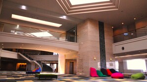 A spacious lobby with a high ceiling, a staircase, and a seating area with colorful cushions. - Satsuma Resort Hotel (Satsuma)