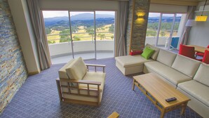 A room with a sofa, a chair, a small table, and a view of a landscape through large windows. - Satsuma Resort Hotel (Satsuma)
