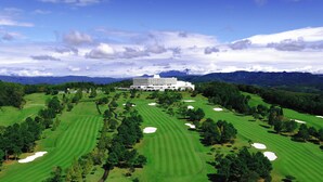 A golf course with a large hotel in the background. - Satsuma Resort Hotel (Satsuma)