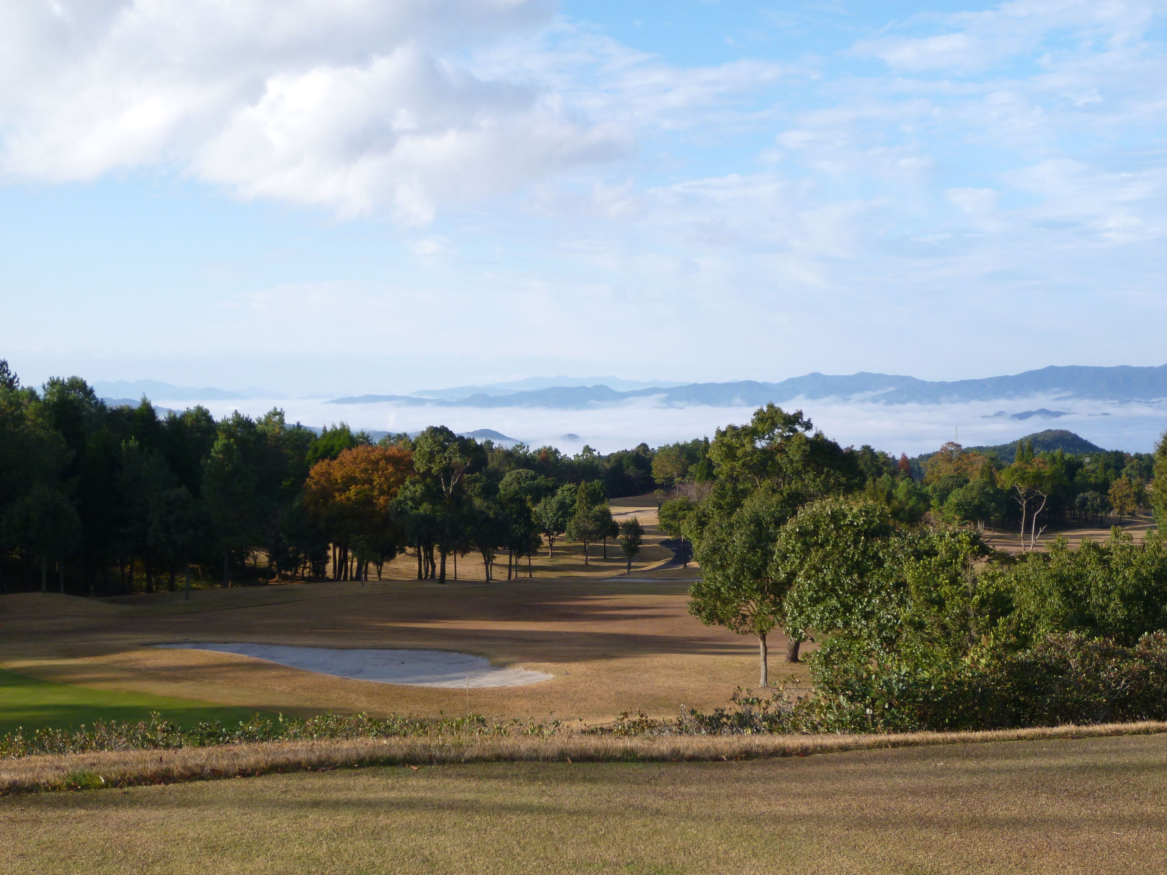 A golf course with a pond, trees, and distant mountains under a clear sky.