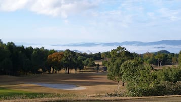 A golf course with a pond, trees, and distant mountains under a clear sky.