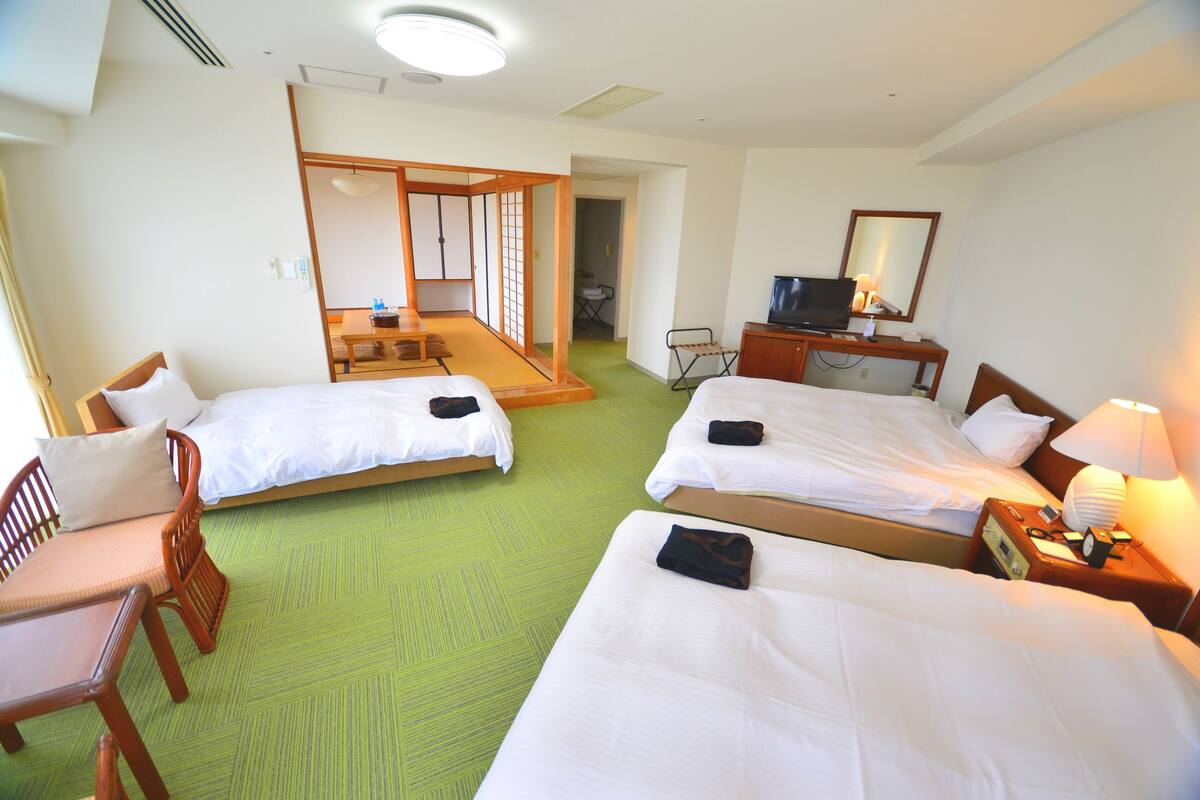 A hotel room with two beds, a desk, a chair, a TV, and a mirror.