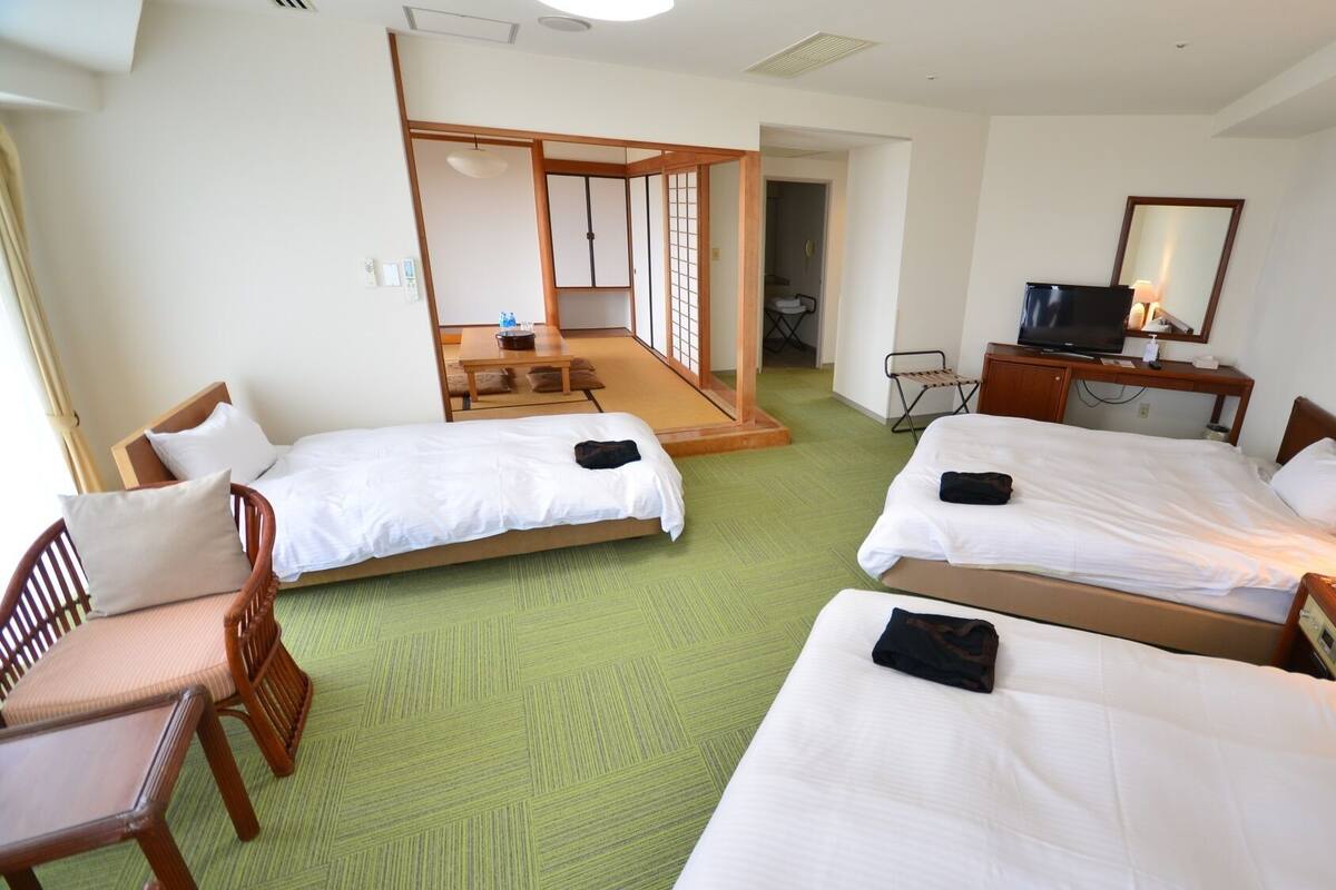 A hotel room with two beds, a desk, a chair, a TV, and a mirror.