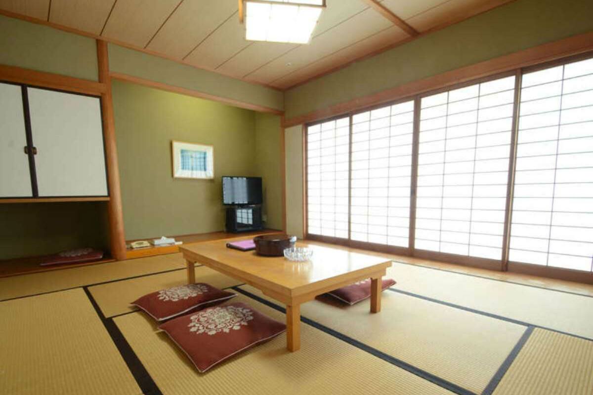 A tatami mat room with a wooden table, cushions, a cabinet, and a large window.