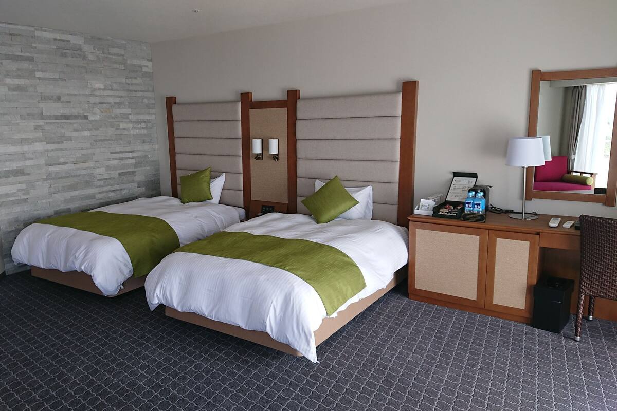 A hotel room with two beds, a desk, a chair, a lamp, and a mirror.