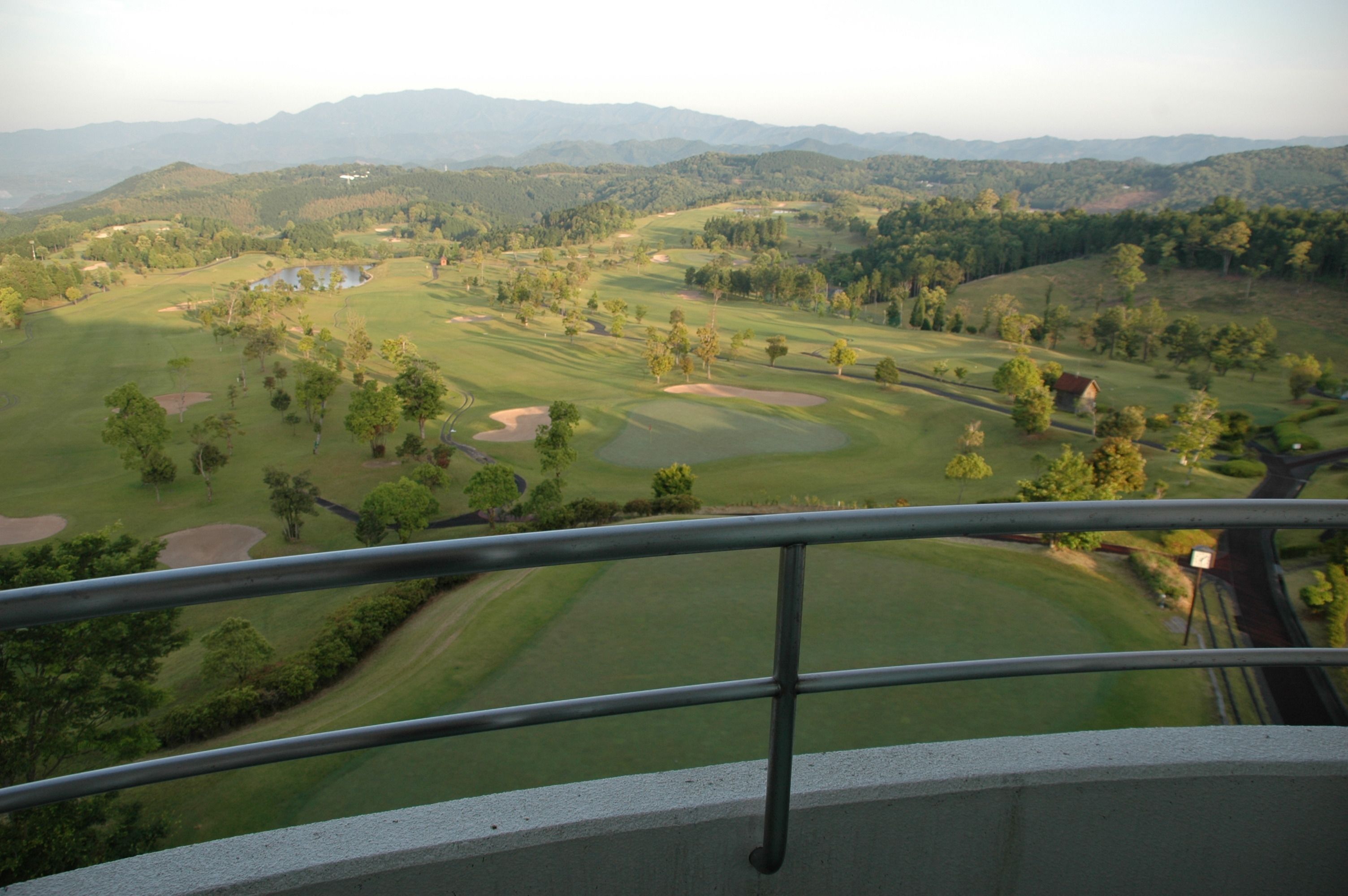 A golf course with bunkers, trees, and distant mountains.