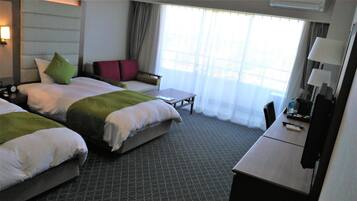 A hotel room with two beds, a small table, a chair, and a desk with a lamp.