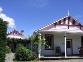 A white building with a red roof and a chimney, surrounded by greenery and a gravel path.
