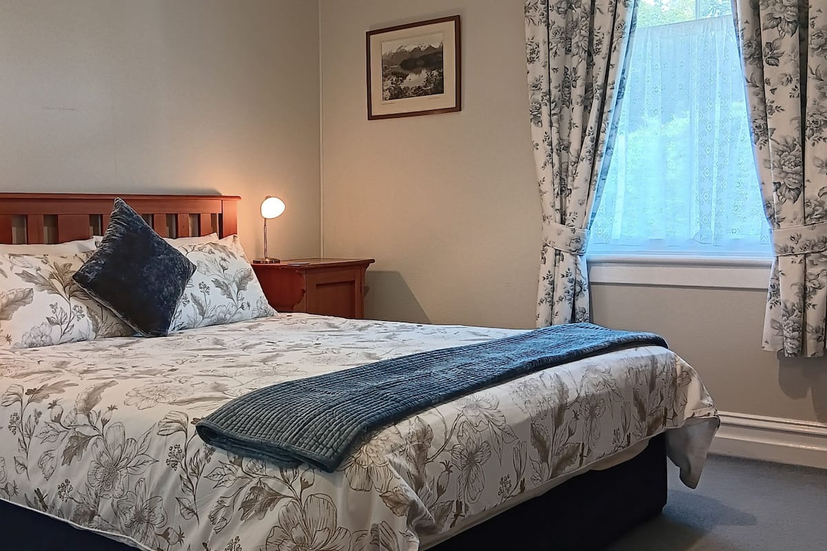 A neatly made bed with floral bedding, two bedside lamps, and a window with floral curtains.