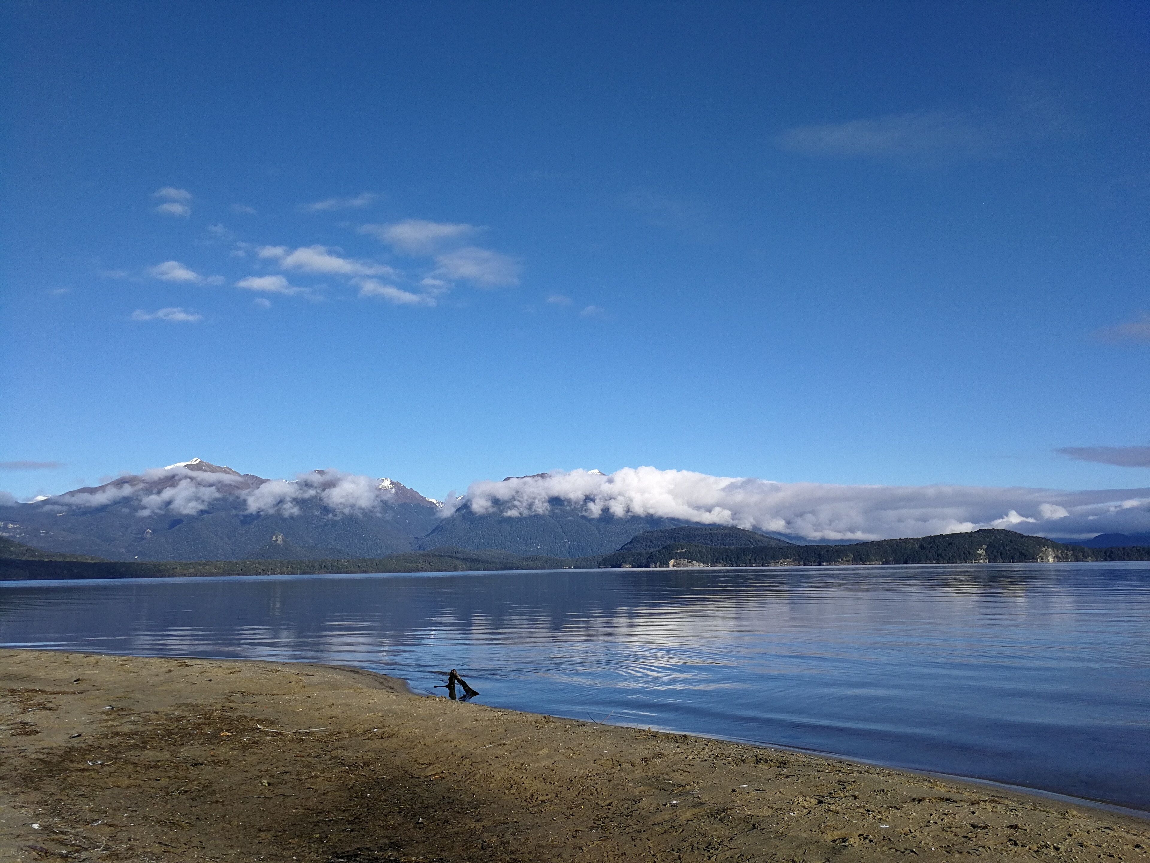 Ein See mit Bergen im Hintergrund und einem Sandstrand im Vordergrund.