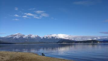 Ein See mit Bergen im Hintergrund und einem Sandstrand im Vordergrund.