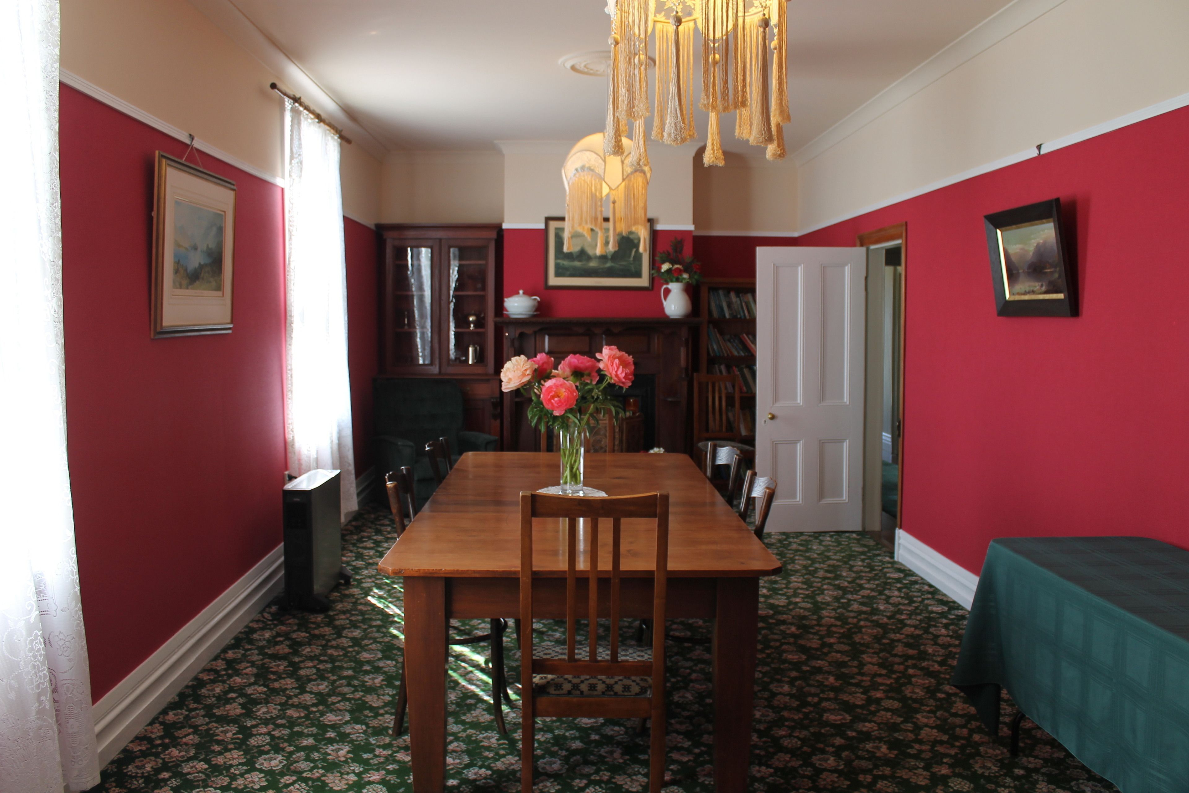 A dining area with a wooden table, chairs, and a vase of flowers. There is a bookshelf and a door in the background.