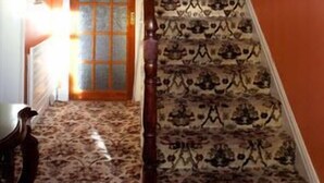 A staircase with patterned carpet leading to a room with a door and a window. - The Orchard (Newcastle West)