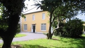 A yellow building with a paved driveway and a tree in the foreground. - The Orchard (Newcastle West)