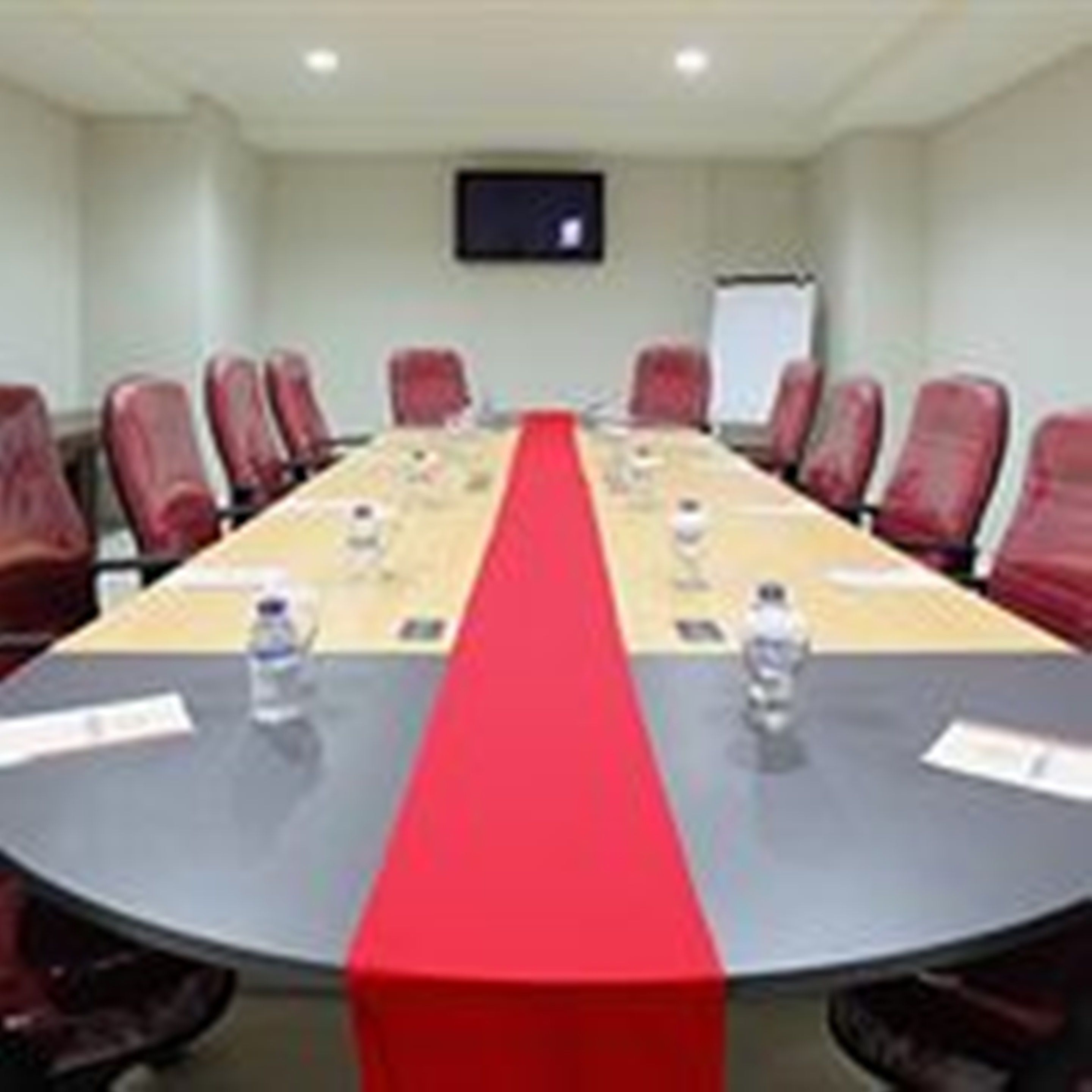 Une salle de conférence avec une longue table, des chaises rouges et un tableau blanc.
