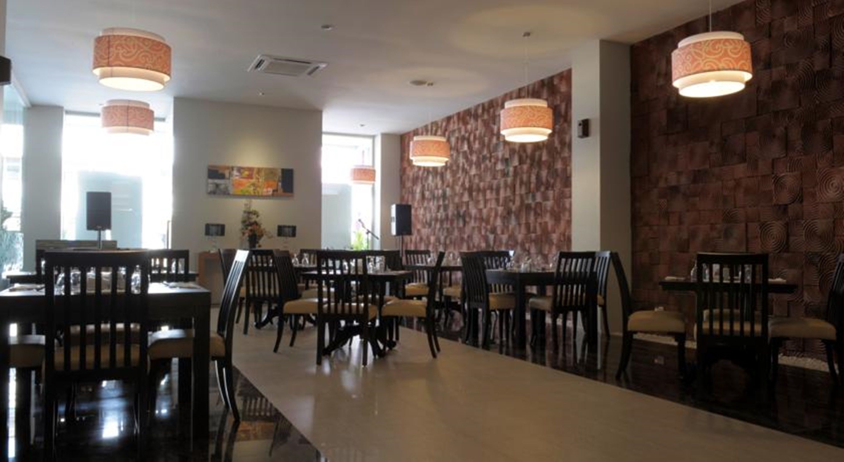 A spacious dining area with multiple tables and chairs, patterned wall, and pendant lighting.