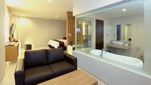 A modern hotel room with a large bed, a sofa, a wooden coffee table, and a large window with a view of the city. - Lombok Plaza Hotel & Convention (Mataram)