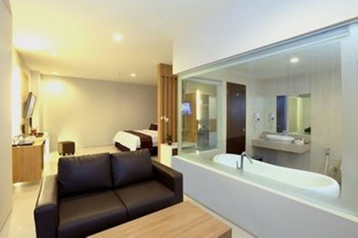 Una habitación de hotel moderna con una cama grande, un sofá, una mesa de centro de madera y un ventanal con vistas a la ciudad.
