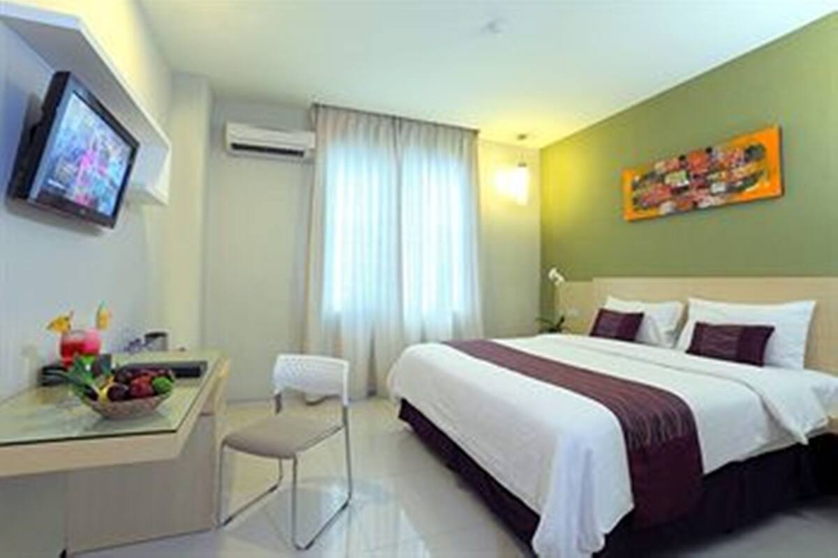 Una habitación de hotel con una cama, un escritorio con computadora, una silla, un televisor y un cuadro en la pared.