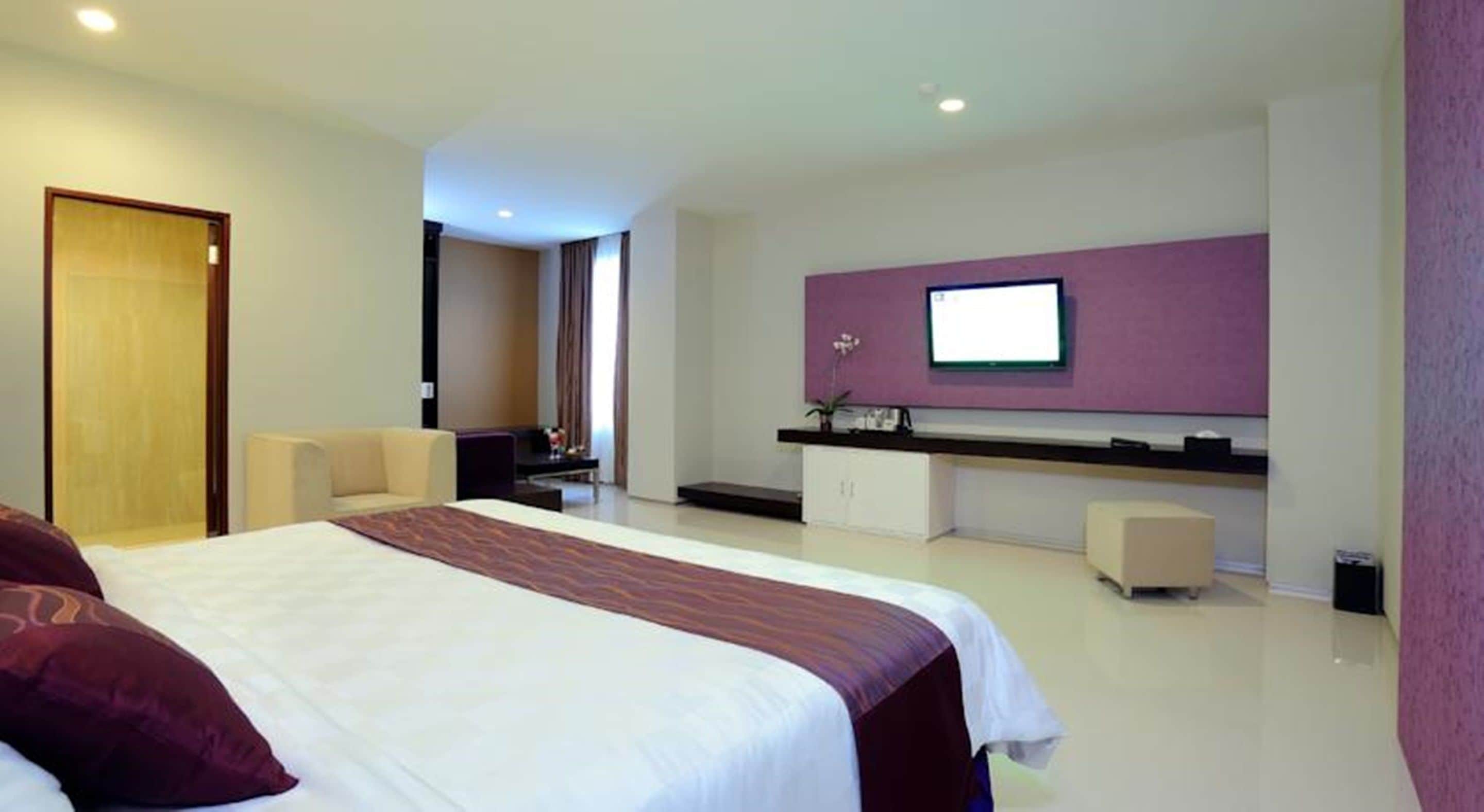Una habitación de hotel moderna con una cama grande, un escritorio y un televisor en la pared.