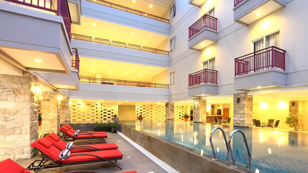 A multi-level indoor pool area with red lounge chairs and a stone wall. - Lombok Plaza Hotel & Convention (Mataram)