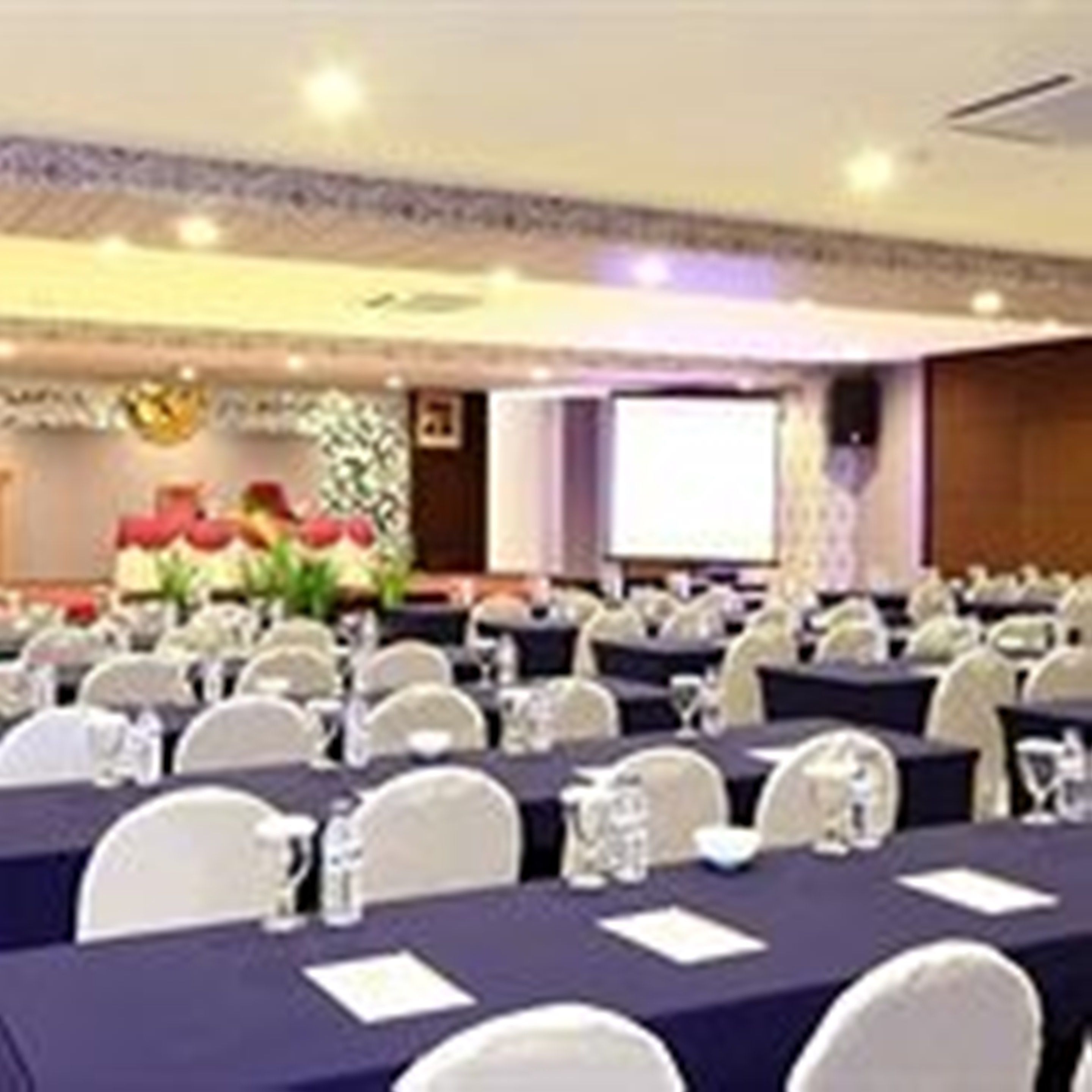Una sala de conferències amb taules rodones, cadires blanques i una pantalla de projector.
