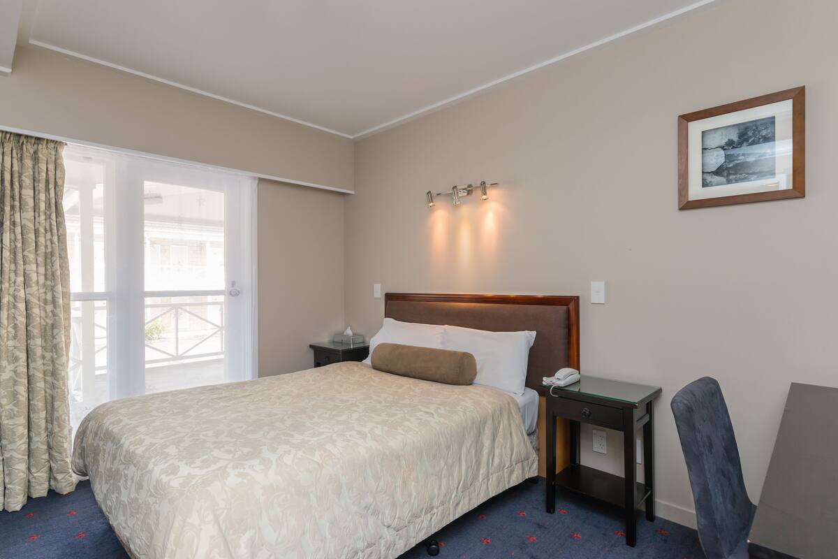 Ein Hotelzimmer mit einem großen Bett, einem Schreibtisch, einem Sessel, einem Nachttisch und einem gerahmten Bild an der Wand.