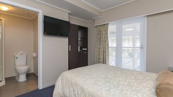 A hotel room with a bed, a television mounted on the wall, a bathroom with a toilet and sink, and a window with curtains.