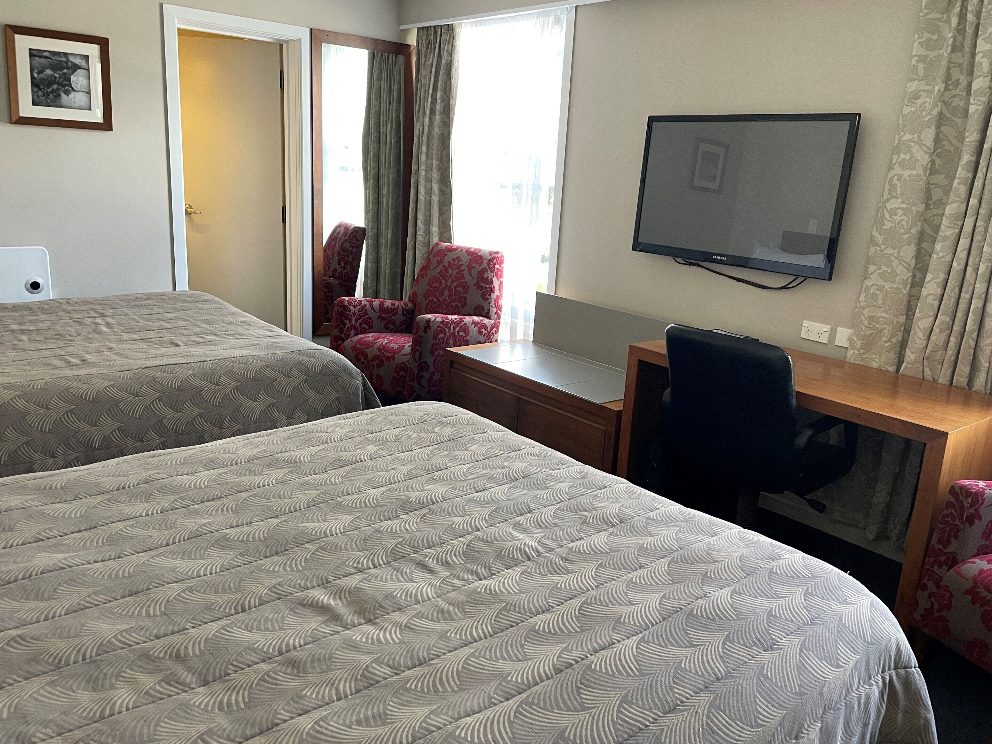 A hotel room with two beds, a desk with a chair, a television, and a window with curtains.