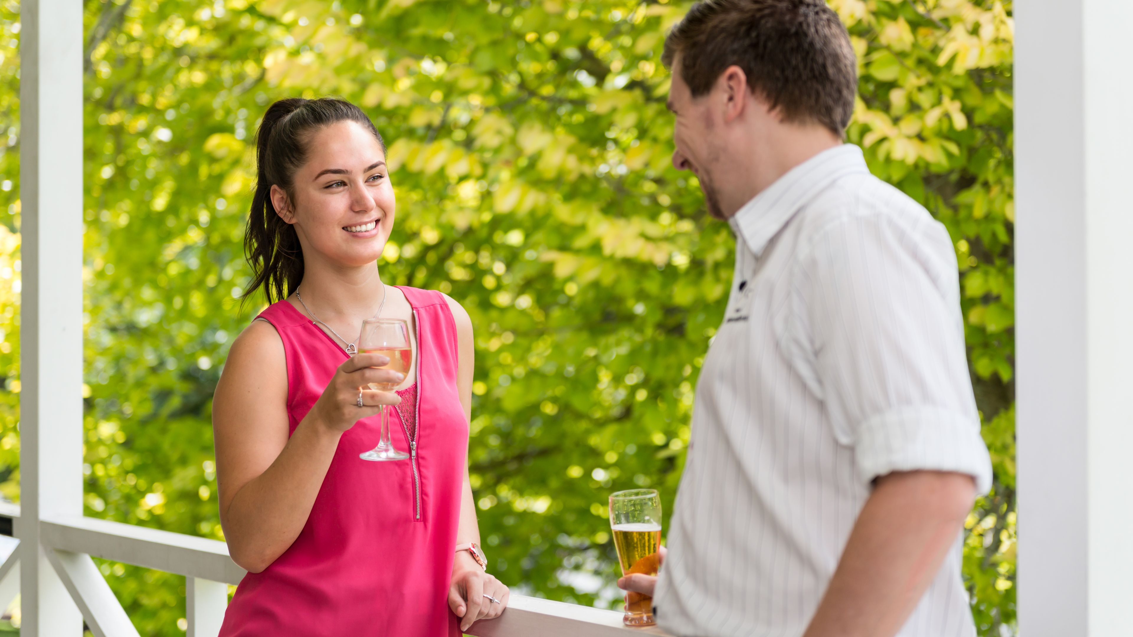 A couple standing on a balcony with a lush green background.