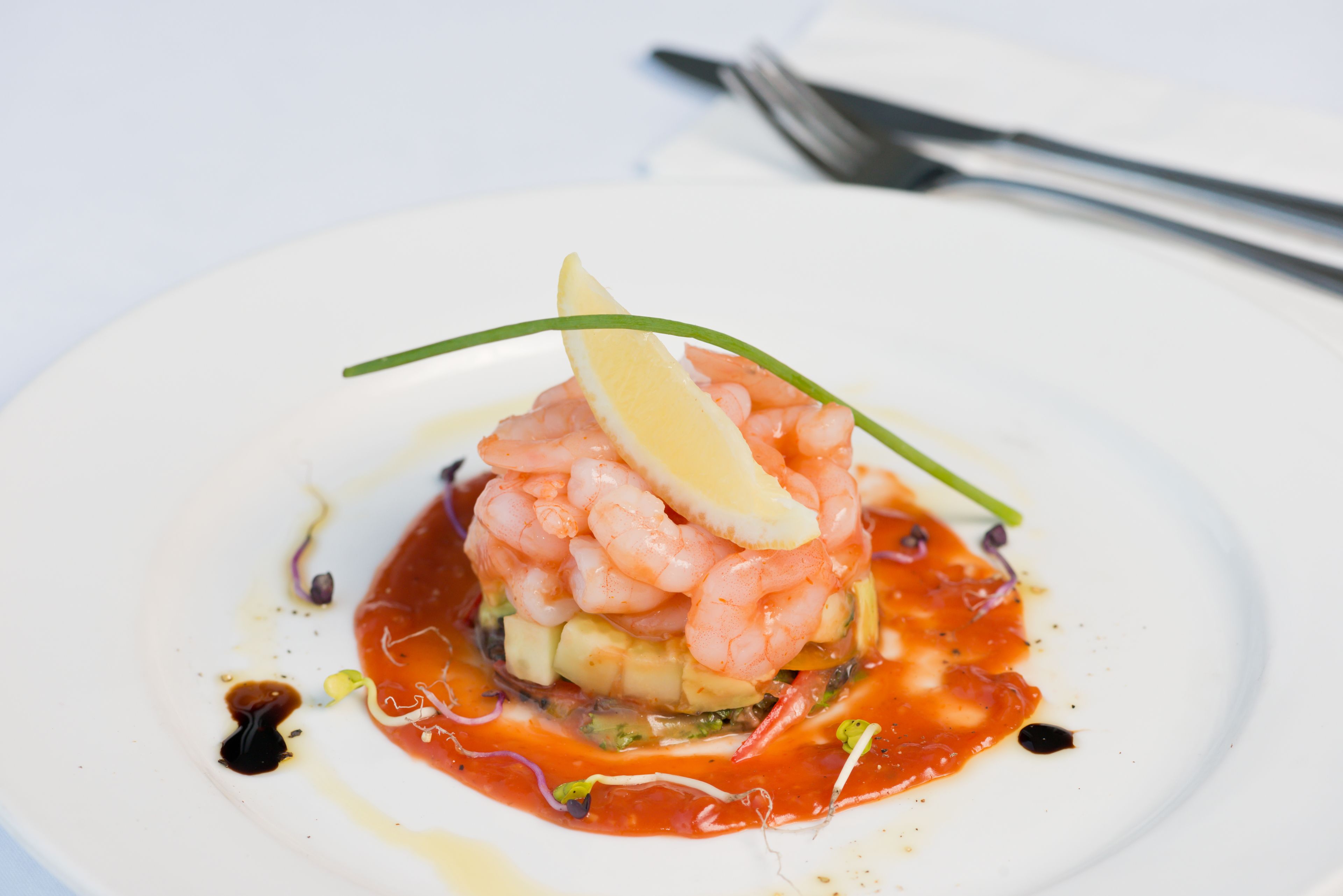 A seafood dish on a white plate with a lemon wedge and green garnish.