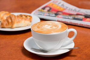 Coffee and pastries are served on a table with a newspaper.