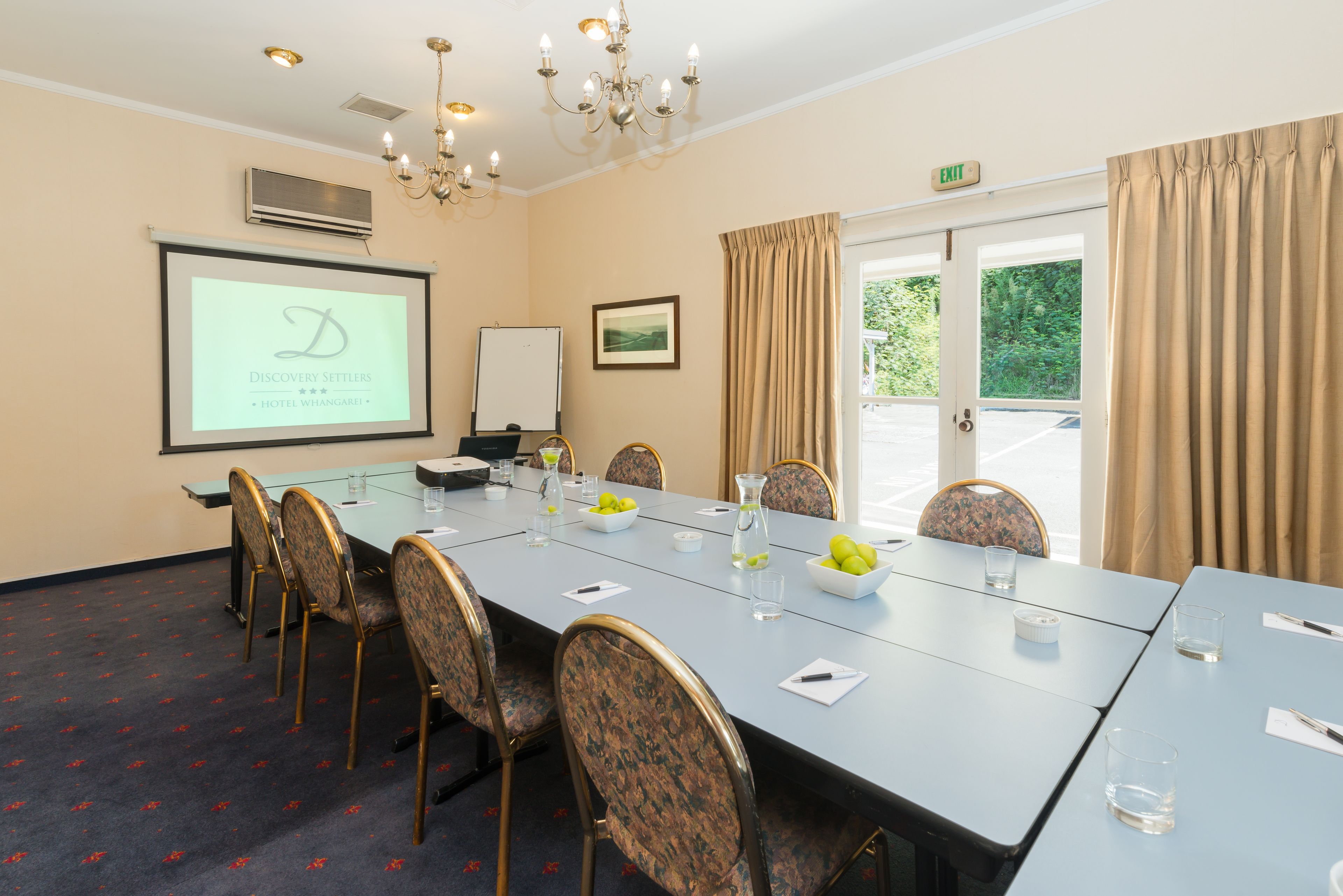 A conference room with a long table, chairs, a projector screen, and a whiteboard.