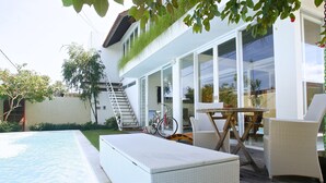 Et moderne udendørsområde med swimmingpool, fletmøbler og en trappe til en overdækket terrasse.