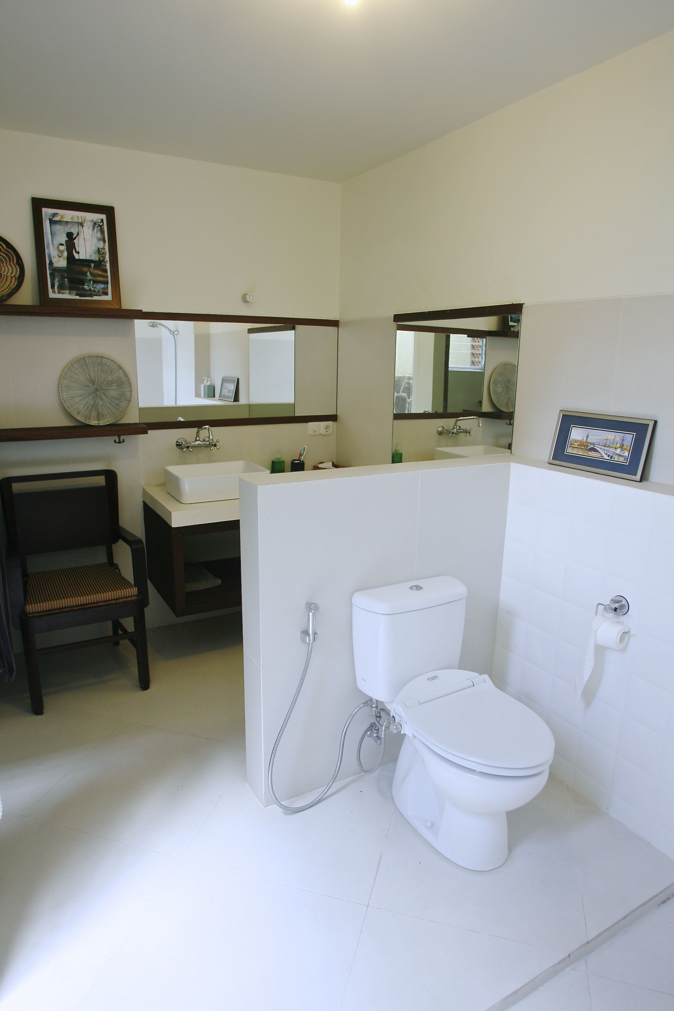 A bathroom with a white sink, a toilet, a chair, and a mirror.