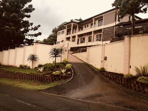 Um edifício com vários andares e um pátio central, rodeado por um muro baixo e diversas plantas.